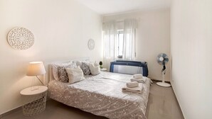 A bedroom with a bed, bedside lamp, and a standing fan. - Apartment 'Matinhos House' with Balcony, Wi-Fi and Air Conditioning (Faro)