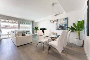 A modern living room with a glass dining table, white sofas, and a large window offering a city view. - Apartment "La Cala Calaserena" with Shared Pool & Wi-Fi (La Cala de mijas)