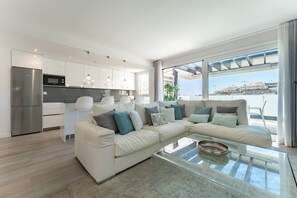 A modern living room with a sofa, a glass coffee table, and a kitchen area with a refrigerator and microwave. - Apartment "La Cala Calaserena" with Shared Pool & Wi-Fi (La Cala de mijas)