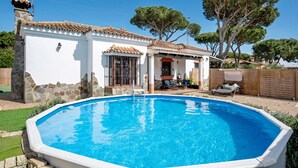 A swimming pool with a tiled deck, a white building with a tiled roof, and a large tree in the background. - Holiday Home "Villa Mami - families only" with Private Mini Pool, 2 Private Terraces and Wi-Fi (Chiclana de la frontera)