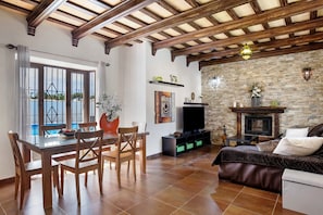 A living room with a dining area, stone fireplace, and a view of the outdoors.