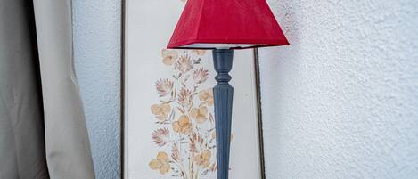 Una obra de arte floral enmarcadas en una pared, una lámpara de pie gris con pantalla roja, y una pared blanca con textura.