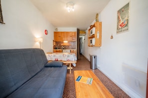 A compact living space with a sofa, a small dining table, a kitchen area, and a trash bin.