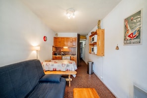 A compact room with a sofa, a small table, a kitchenette, and a bed.
