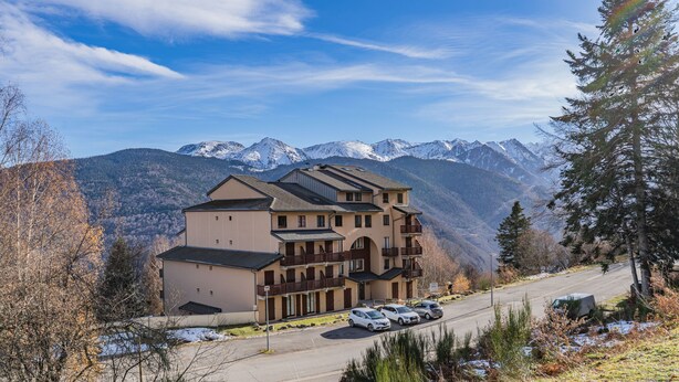 A multi-story building with a parking area and a view of snow-capped mountains. - Studio "Cabine Ax Les 3 Domaines" in a Quiet Setting Near the Slopes (Ax-les-Thermes)