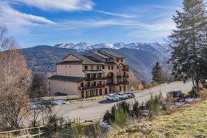 A multi-story building with a parking area and a view of snow-capped mountains.