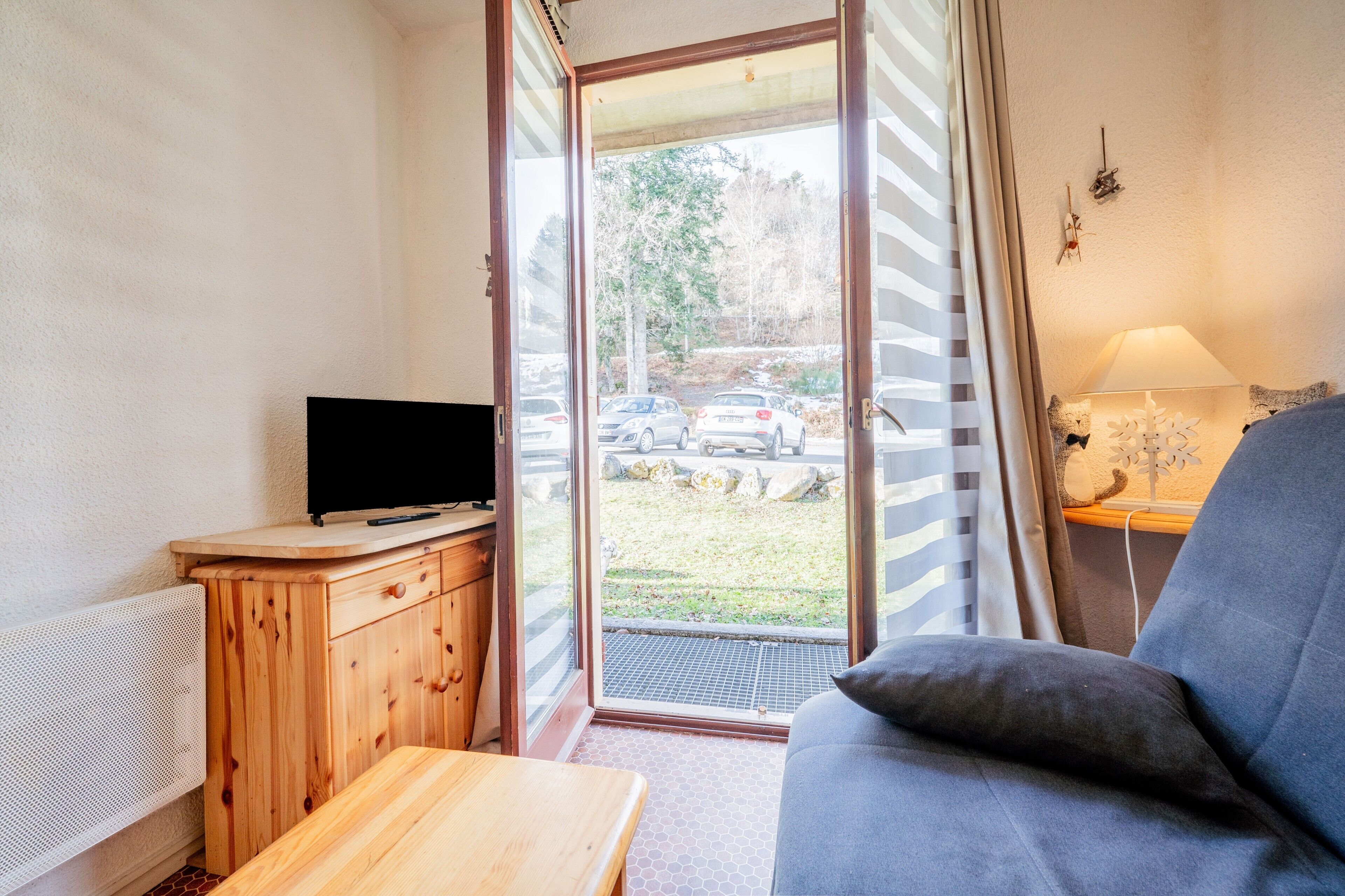 Une pièce comprenant un meuble en bois, une télévision, un canapé et une porte donnant sur l’extérieur.