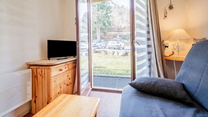 A room with a wooden cabinet, a television, a sofa, and a door leading outside. - Studio "Cabine Ax Les 3 Domaines" in a Quiet Setting Near the Slopes (Ax-les-Thermes)