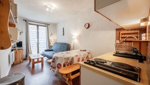 A compact room with a bed, a small table, a bench, a kitchenette, and a window with blinds. - Studio "Cabine Ax Les 3 Domaines" in a Quiet Setting Near the Slopes (Ax-les-Thermes)