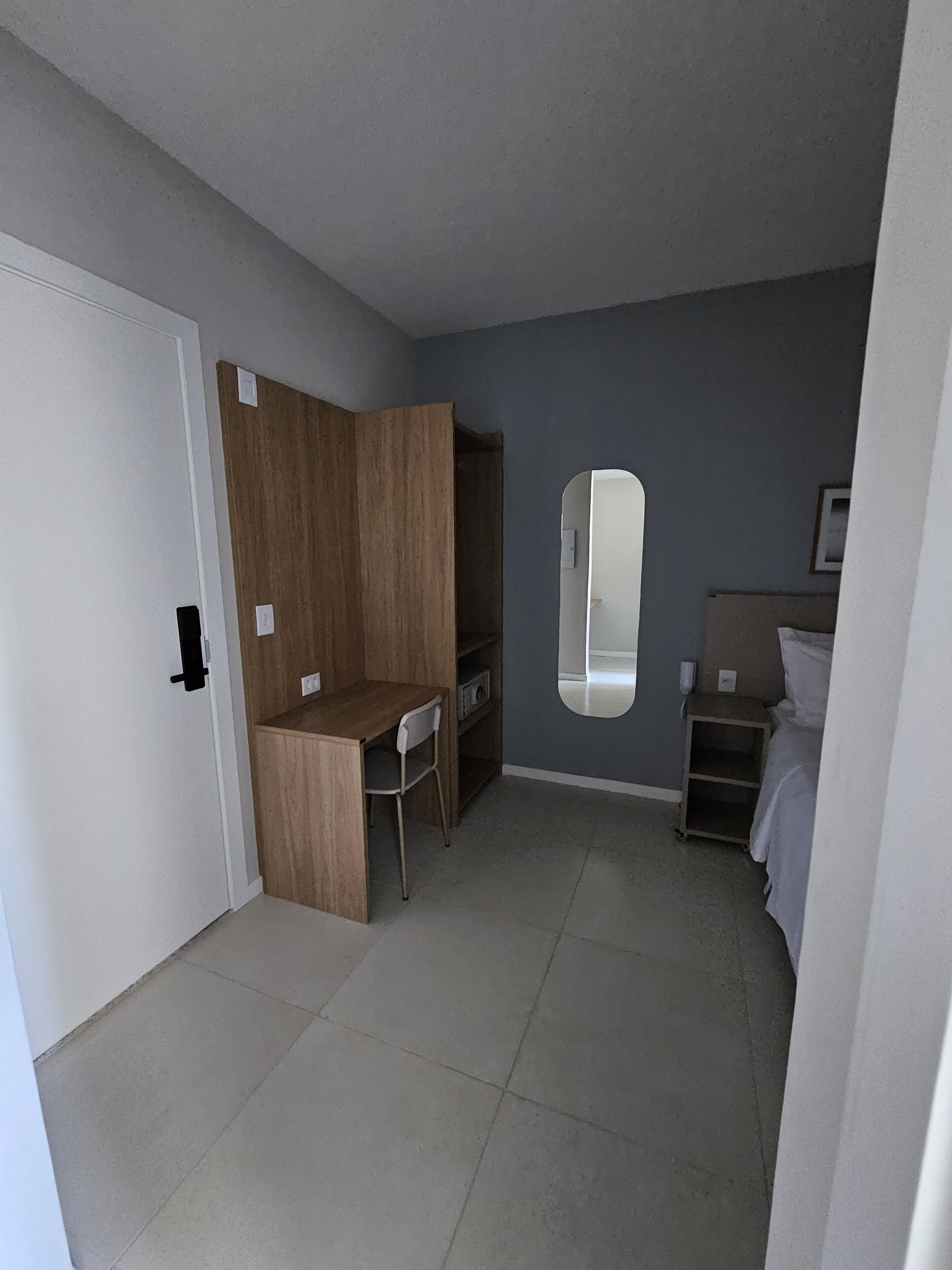 Una habitación pequeña y funcional con escritorio de madera, una silla, una cama y una mesita de noche.