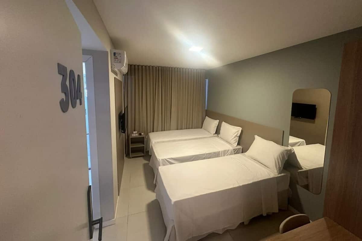 A hotel room with two beds, a small table, a chair, a mirror, and a TV.
