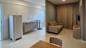Ein modernes, helles Wohnzimmer mit Couch, Holztisch und einer Küche im Hintergrund.