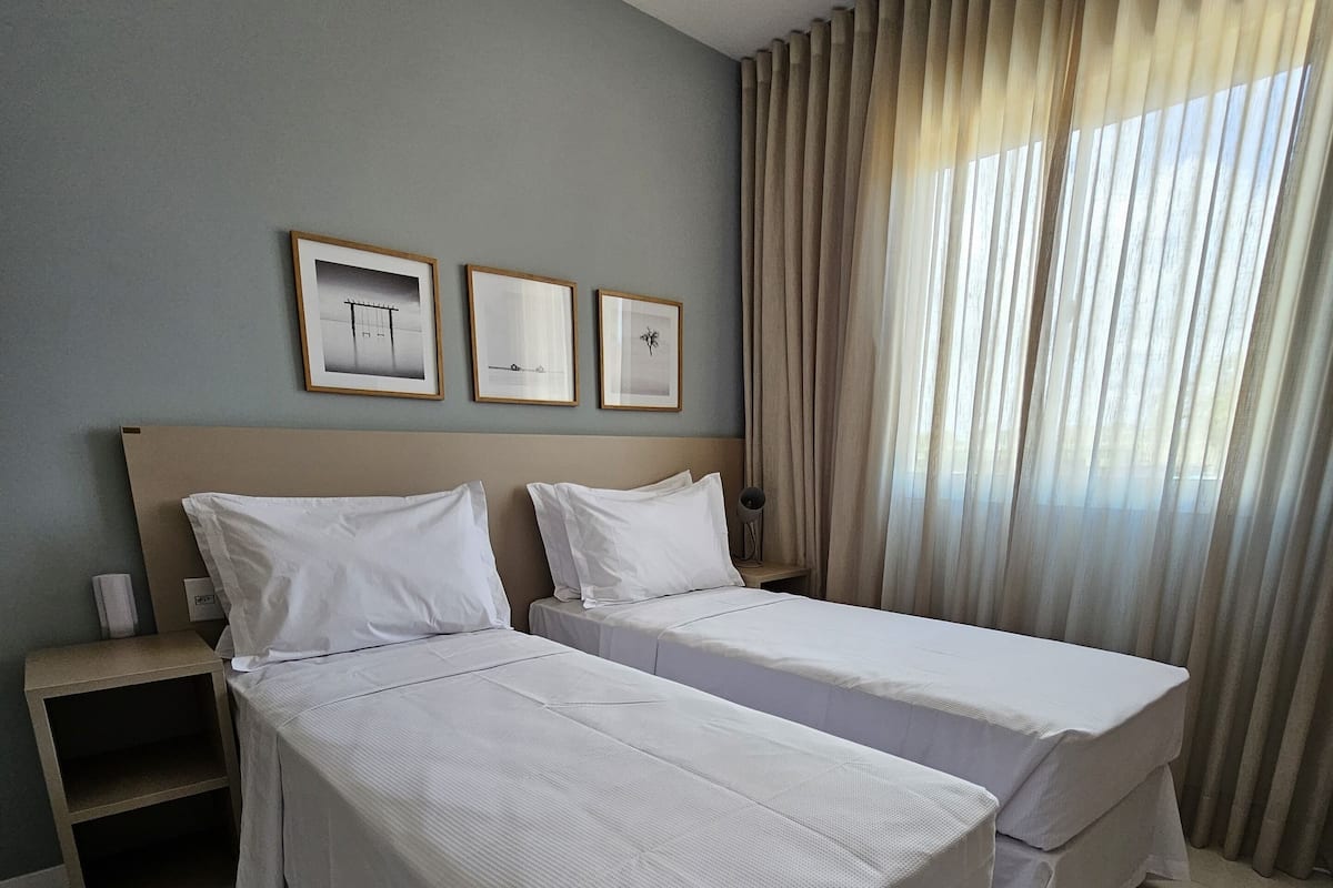 A hotel room with two beds, a nightstand, and a window with curtains.