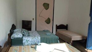 A bedroom with two beds, one larger and one smaller, both with wooden frames. There is a dresser and a wall-mounted fan.