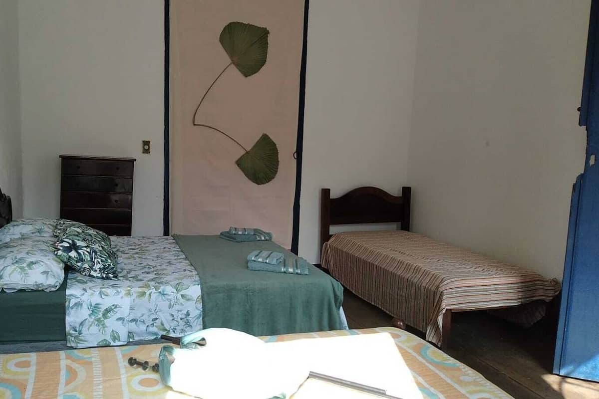 A bedroom with two beds, one larger and one smaller, both with wooden frames. There is a dresser and a wall-mounted fan.