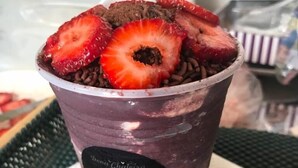 A purple beverage cup with a straw, topped with strawberries, on a table with a placemat.