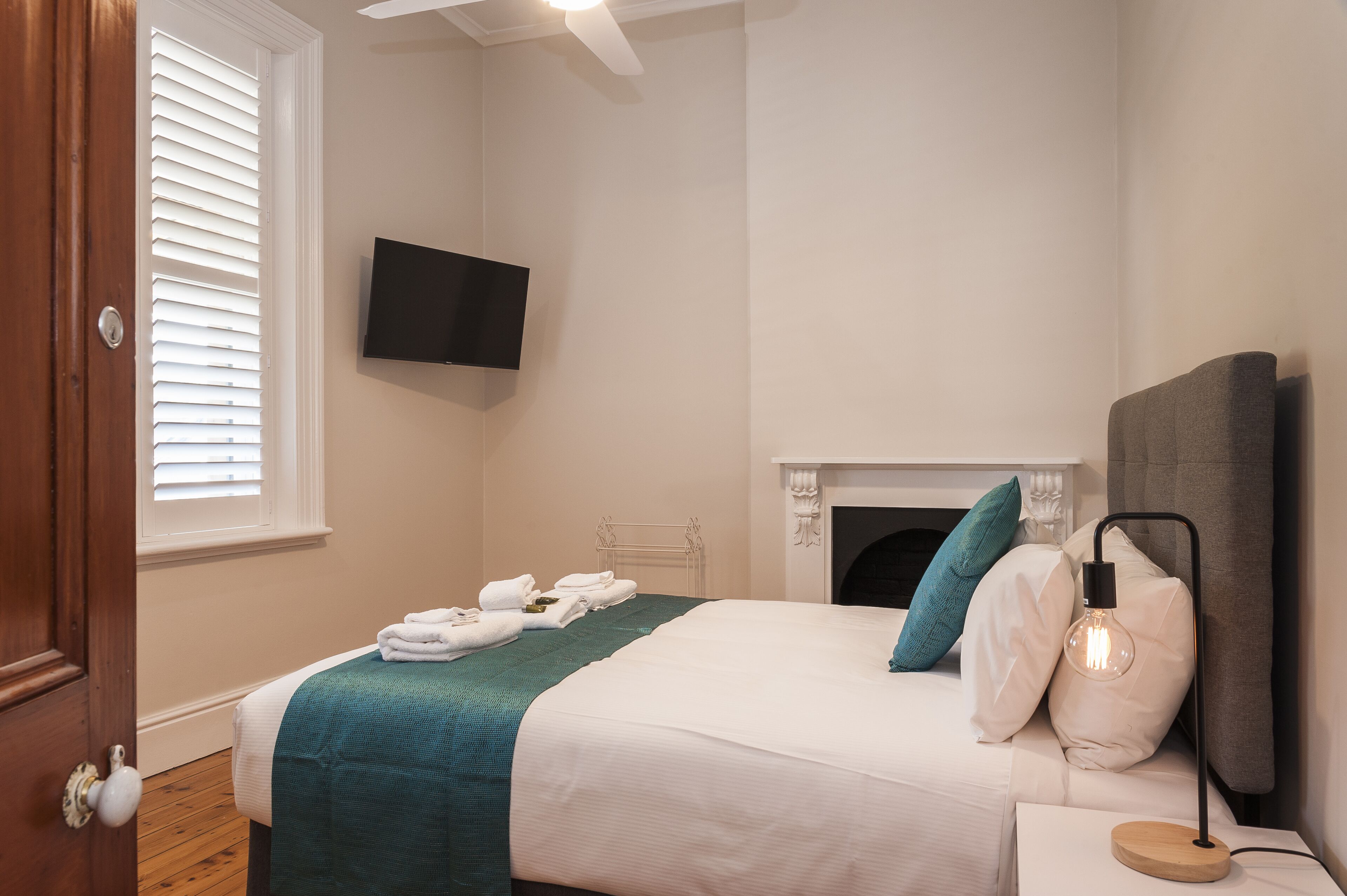 A bedroom with a bed, a television mounted on the wall, a fireplace, and a bedside table with a lamp.