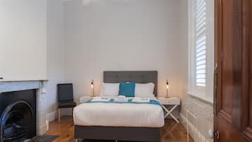 Un dormitorio con cama, mesitas de noche, chimenea y ventana con persianas.