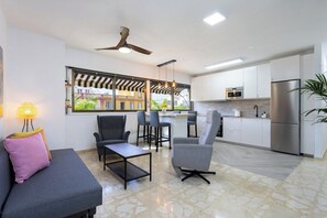 A modern kitchen with white cabinets, a stainless steel refrigerator, and a dining area with a sofa and chairs.
