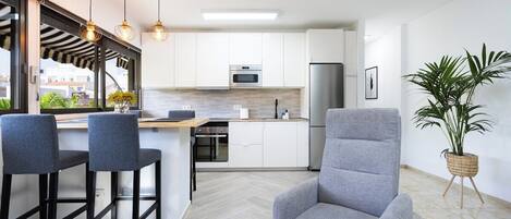 Una cocina moderna con armarios blancos, un refrigerador de acero inoxidable y una zona de bar con taburetes.