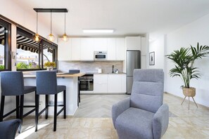 A modern kitchen with white cabinets, a stainless steel refrigerator, and a bar area with stools.