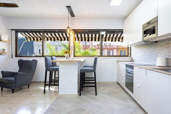 A modern kitchen with a central island, bar stools, and a view through large windows.