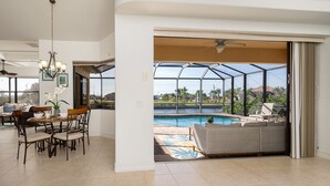 Ein geräumiger Wohnbereich mit Esstisch, Deckenventilator und Blick auf einen Swimmingpool durch eine Glasfassade.