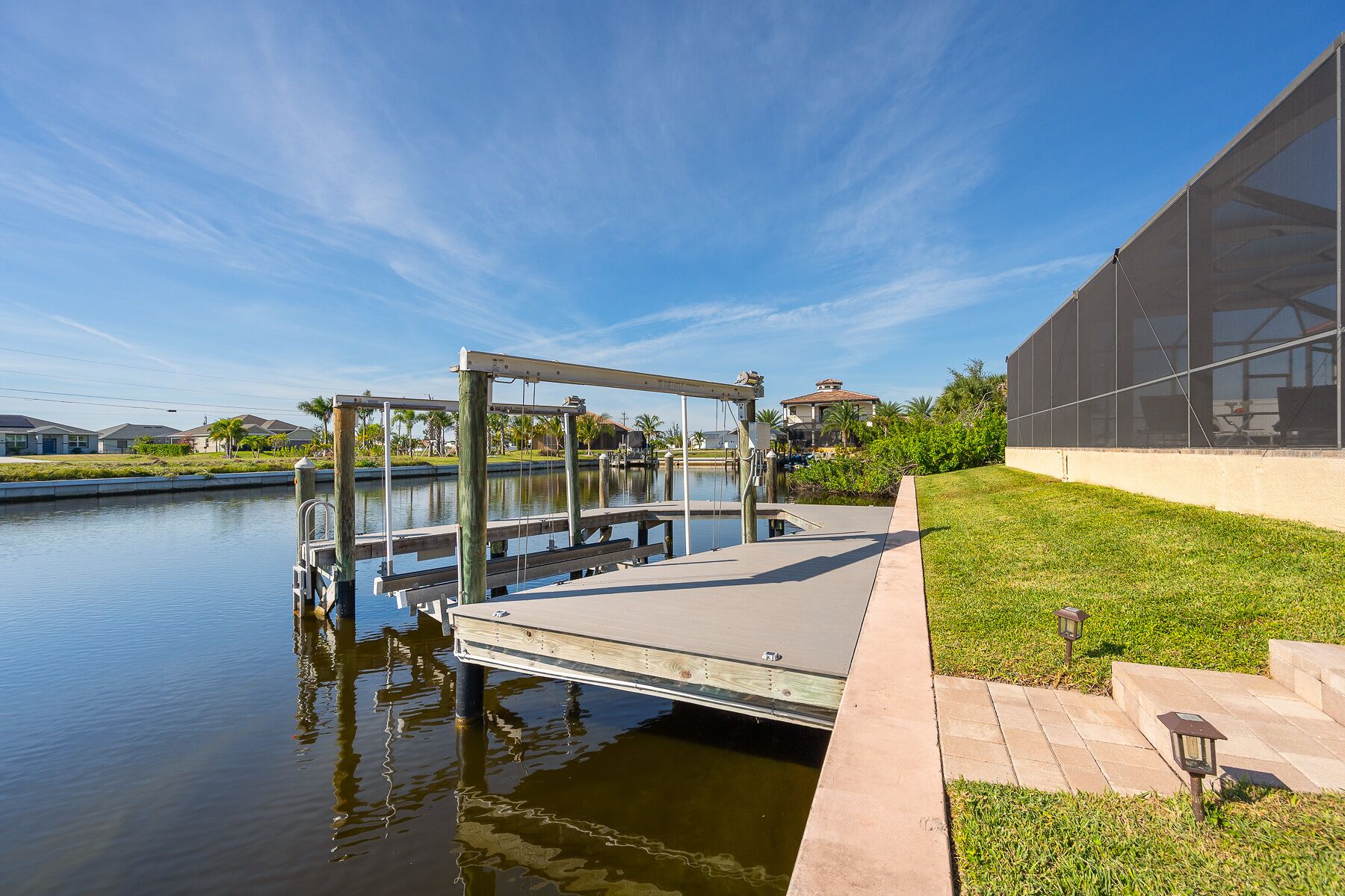 A dock extending into a calm body of water, with a grassy area and a modern building with large windows on the right.