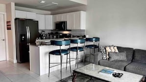 Una cocina moderna con armarios blancos, un refrigerador de acero inoxidable y una zona de bar con taburetes azules.