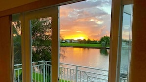 Un balcón con vistas a un atardecer sobre un lago, una mesa, sillas y una barandilla.