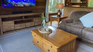 Una sala de estar acogedora con un mueble bajo de televisión de madera, un sofá de cuero, una mesa de centro de madera y una ventana con cortinas.