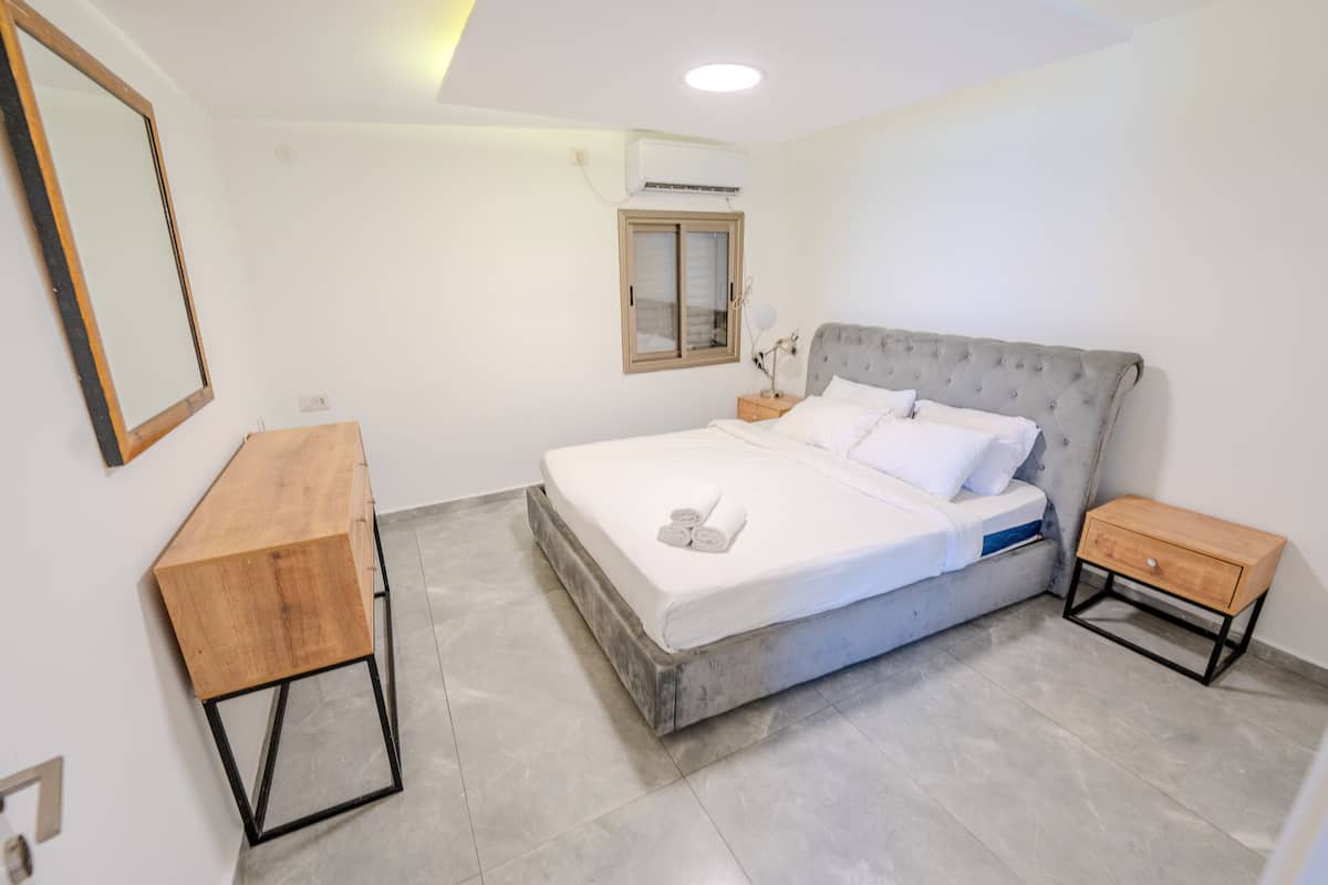 Une chambre moderne avec un grand lit, une table de chevet en bois, une petite table de nuit, un miroir et un appareil de climatisation.