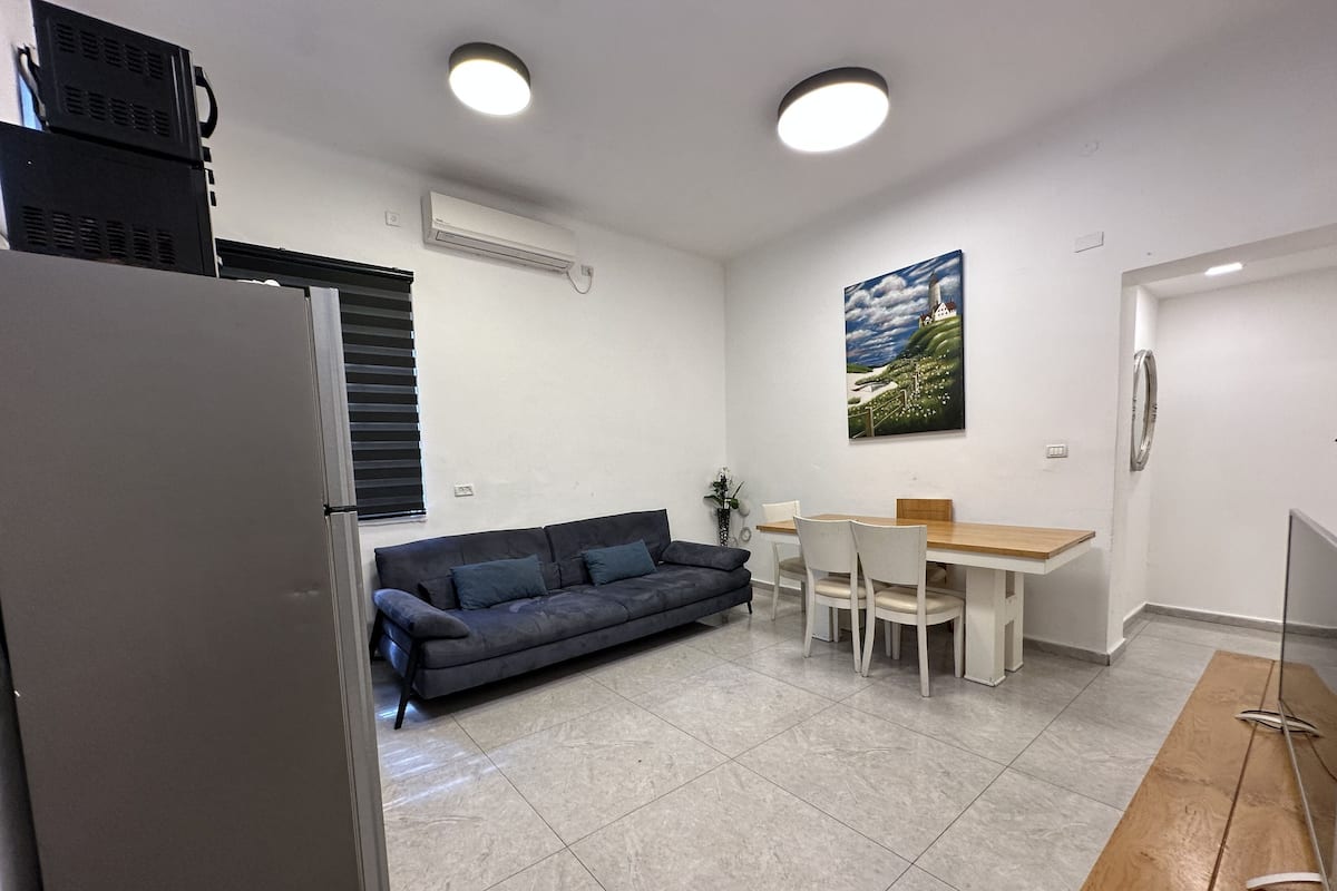 Une cuisine de taille réduite comprenant un réfrigérateur, un canapé foncé, une table à manger avec des chaises et un tableau accroché au mur.