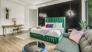 Een moderne slaapkamer met een met groen bekleden bed, een bureau met een lamp, een stoel, een blauwe ronde fauteuil en een groot raam.