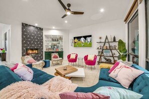 A modern living room with a sofa, chairs, a coffee table, a fireplace, a TV, and a bookshelf. - Flamingo Palms: Pool, Spa, Pet-Friendly, Games! (Indio)