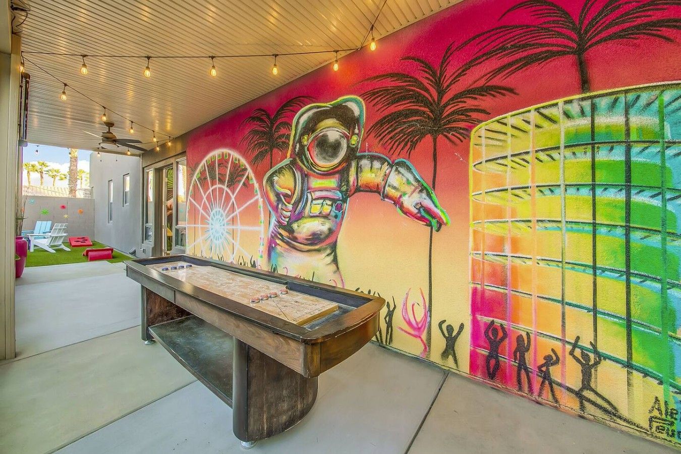 A pool table in a room with a vibrant mural on the wall, including a large astronaut figure and palm trees.