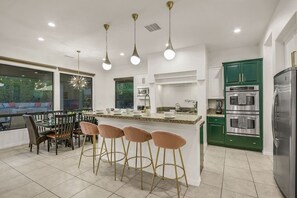 A modern kitchen with a central island, bar stools, a dining table, and green cabinetry. - Flamingo Palms: Pool, Spa, Pet-Friendly, Games! (Indio)