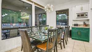 Een eetgedeelte met een glazen tafel, stoelen en uitzicht op de omgeving. Er is een keuken met witte kasten en een groen aanrecht.