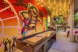 A room with a shuffleboard table, a mural with abstract art, and a television screen displaying a program. - Flamingo Palms: Pool, Spa, Pet-Friendly, Games! (Indio)