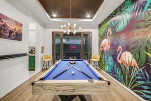 Une table de billard, un néon, un lustre et une fresque murale aux couleurs vives.