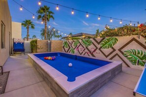 An outdoor pool area with a blue pool, a basketball hoop, and string lights. - Flamingo Palms: Pool, Spa, Pet-Friendly, Games! (Indio)