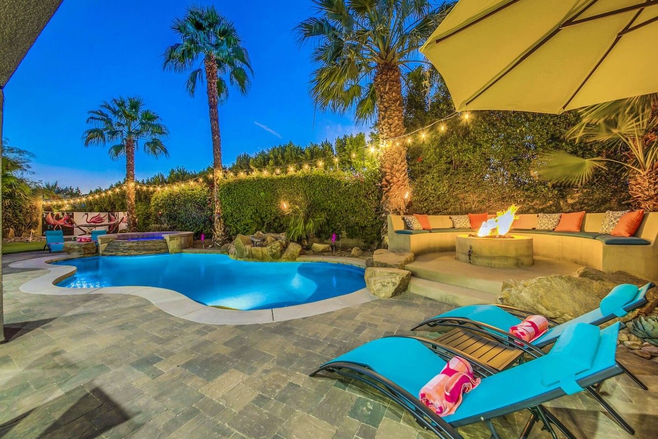 A pool area with lounge chairs, a fire pit, and string lights.
