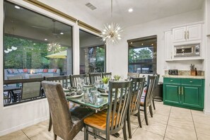 A dining area with a glass table, chairs, and a view of the outdoors. - Flamingo Palms: Pool, Spa, Pet-Friendly, Games! (Indio)
