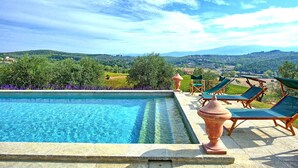 Une piscine à l’eau d’un bleu cristallin, entourée d’une terrasse agrémentée de chaises longues, d’où l’on peut admirer des collines verdoyantes et des vignobles.