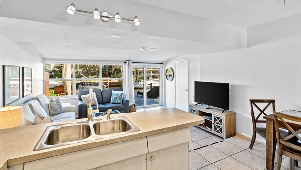 Et moderne køkken med en stor ø, et spiseområde med et træbord og stole, et indbygget tv og en siddeplads med en sofa og sofabord.
