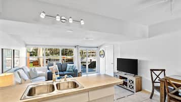 A modern kitchen with a large island, a dining area with a wooden table and chairs, a built-in TV, and a seating area with a sofa and a coffee table.