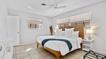A bedroom with a bed, a ceiling fan, a bedside table with a lamp, and a window with blinds.