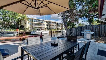 An outdoor patio with a table and chairs, a grill, and a view of a marina with boats and buildings in the background.