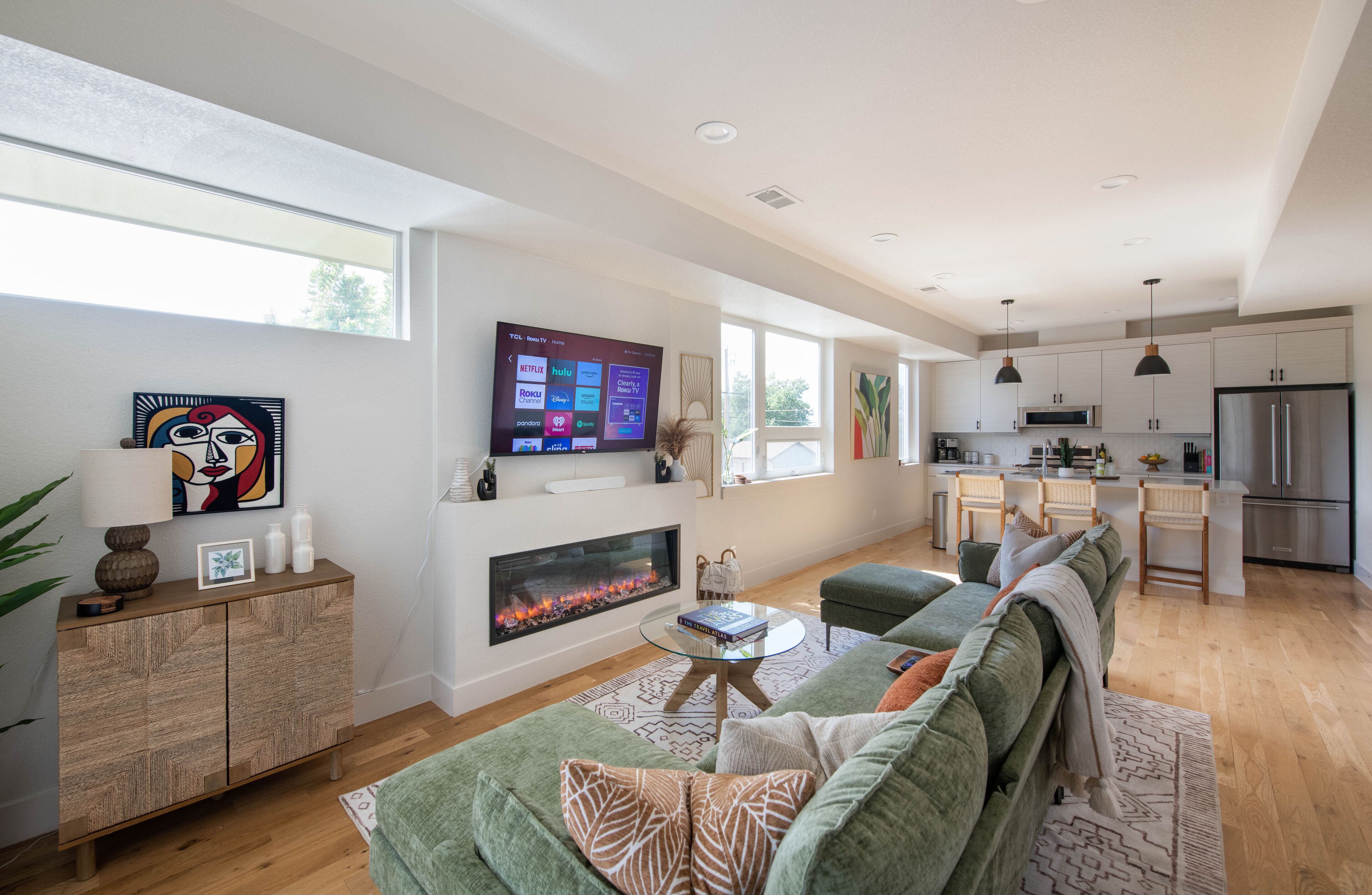 A modern living room with a fireplace, green sofa, and a flat-screen TV mounted on the wall.