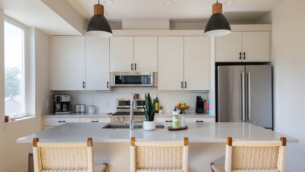 A modern kitchen with light wood cabinets, stainless steel appliances, and a central island with wicker chairs. - New townhome with private rooftop deck and beautiful Mountain Views, 5 min to DU (Denver)